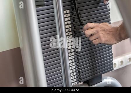 La main de l'homme changer le poids lourd sur les plaques de fer empilés poids machine avec kilogramme nombre dans fitness gym Banque D'Images