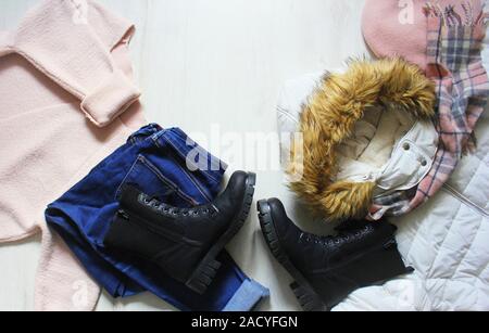 Un ensemble d'hiver à la mode des vêtements de femmes. Chandail de laine, chaussures, jeans, manteau, chapeau et un foulard blanc sur fond de bois. Banque D'Images