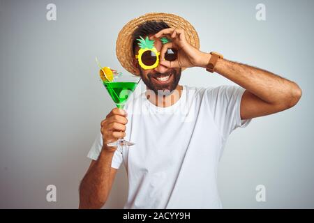 L'été indien homme portant un regard amusé cocktail sur fond blanc isolé avec happy smiling face ok faire signer avec la main sur l'œil à la t Banque D'Images