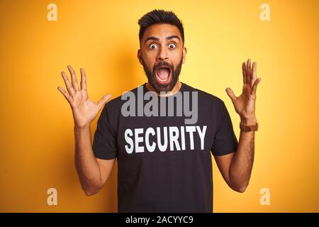 Sauvegarde hispanique indienne arabe homme portant un uniforme de sécurité sur fond jaune isolé célébrant la folie et surpris du succès avec bras levés Banque D'Images