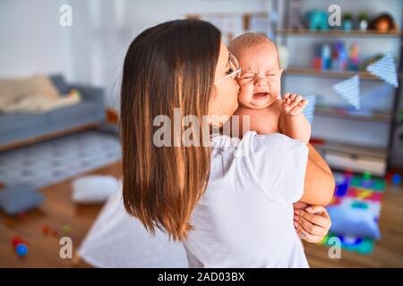 Belle jeune femme et son bébé debout à la maison. Mother holding et d'embrasser le nouveau-né pleure Banque D'Images