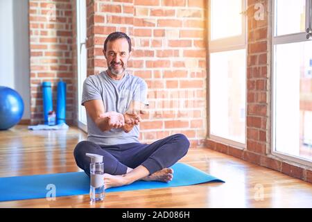 L'âge moyen beau velo assis sur mat doing stretching exercice de yoga à gym Smiling avec mains paumes ensemble la réception ou le geste de donner. Tenir Banque D'Images