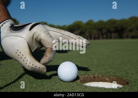 La main de l'homme mettre dans le trou de balle de golf Banque D'Images