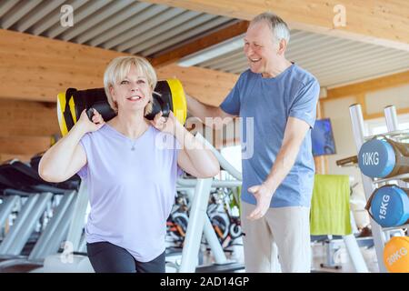 Senior woman doing squats dans le gymnase avec son mari à regarder Banque D'Images