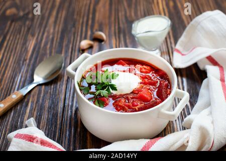 Traditionnelle soupe de betteraves bortsch ukrainien et russe, une cuisine nationale. Bortsch servi dans un bol avec la crème fraîche et le persil sur une table en bois Banque D'Images