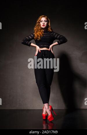 Red-haired woman posing contre du mur noir à la lumière Banque D'Images