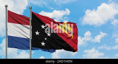 Pays-bas et de brandir le drapeau de la Papouasie-Nouvelle-Guinée dans le vent contre ciel bleu nuageux blanc ensemble. Concept de diplomatie, de relations internationales. Banque D'Images