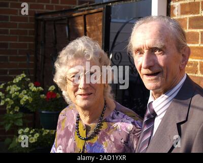 Un couple de retraités dans leur jardin en souriant et en regardant la caméra. Banque D'Images