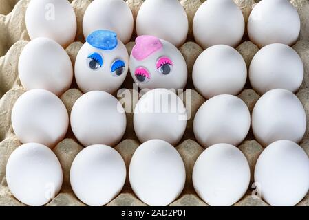 Oeufs mignon avec le visage, les yeux, le museau. Deux œufs avec amour pour l'autre sur des œufs blancs de poulet en fond de cage en carton. Banque D'Images