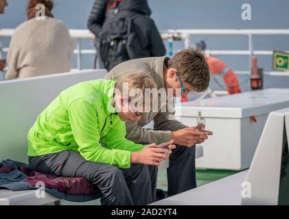 Les adolescents en utilisant leur téléphone cellulaire sur le ferry boat, Baldur, Breidafjordur, Islande Westfjords Banque D'Images