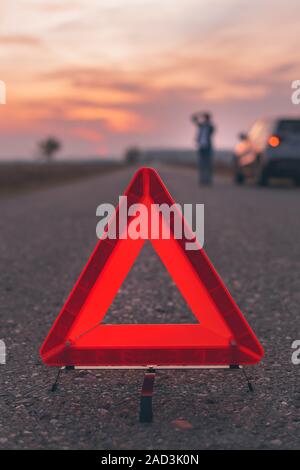 Triangle d'avertissement panneau sur la route, en arrière-plan flou femme appelant à l'assistance routière par la rupture de la voiture, selective focus Banque D'Images