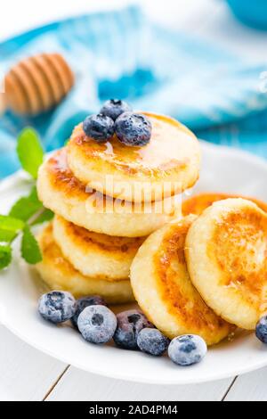 Crêpes de fromage cottage avec du miel et de bleuets sur fond blanc, le petit déjeuner et déjeuner Banque D'Images