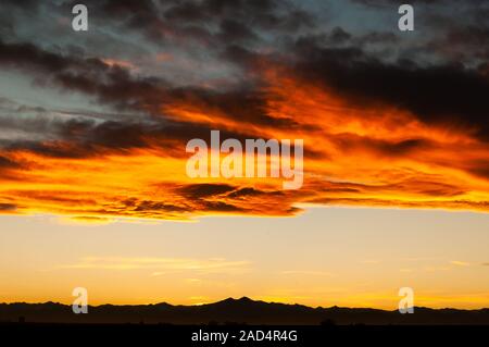 Belles teintes jaune et orange dans les nuages que le soleil se couche derrière les montagnes Rocheuses. Banque D'Images