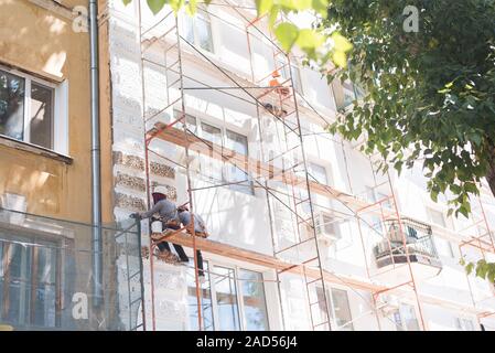 Un homme est assis sur un et restaure le bâtiment. Le constructeur peint les murs de l'édifice et la façade à une hauteur. Banque D'Images