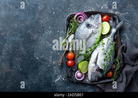 Poisson cru frais Dorado ou dorade avec des ingrédients pour la cuisine sur fond sombre, vue du dessus Banque D'Images