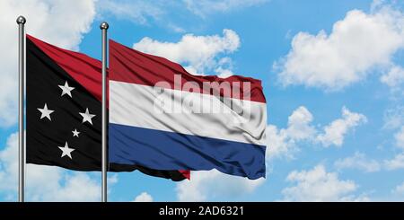 La Papouasie-Nouvelle-Guinée et de brandir le drapeau des Pays-Bas dans le vent contre ciel bleu nuageux blanc ensemble. Concept de diplomatie, de relations internationales. Banque D'Images