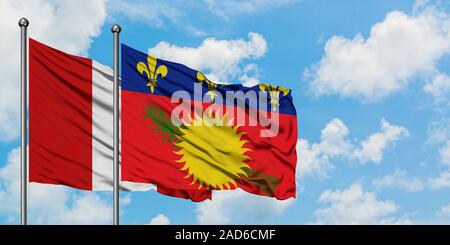 Le Pérou et la Guadeloupe drapeaux dans le vent contre ciel bleu nuageux blanc ensemble. Concept de diplomatie, de relations internationales. Banque D'Images