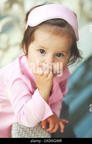 Cute little girl en pyjama, souriant se tient près d'une table avec des fleurs sur un balcon de l'hôtel en été Banque D'Images