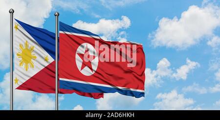 Les Philippines et la Corée du Nord drapeaux dans le vent contre ciel bleu nuageux blanc ensemble. Concept de diplomatie, de relations internationales. Banque D'Images