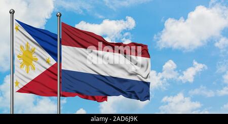 Philippines et de brandir le drapeau des Pays-Bas dans le vent contre ciel bleu nuageux blanc ensemble. Concept de diplomatie, de relations internationales. Banque D'Images