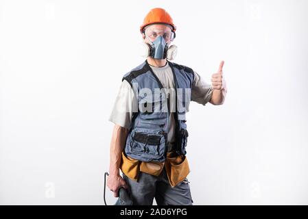 Builder avec une perceuse perforateur, dans un casque, et d'un respirateur. Showing Thumbs up Banque D'Images