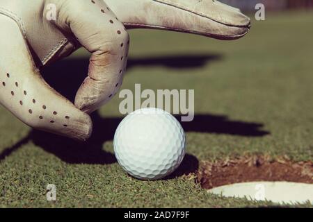 La main de l'homme mettre dans le trou de balle de golf Banque D'Images