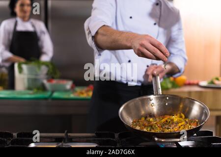 Chef putting épices sur les légumes dans le wok Banque D'Images