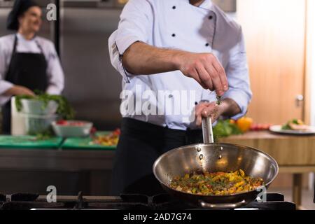 Chef putting épices sur les légumes dans le wok Banque D'Images