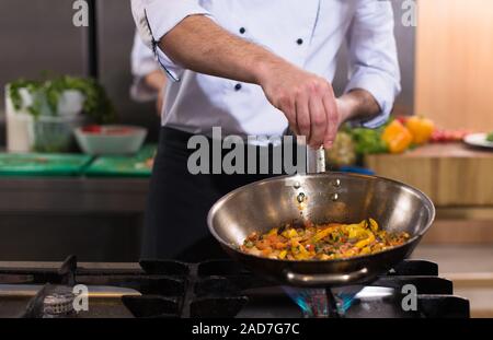 Chef putting épices sur les légumes dans le wok Banque D'Images