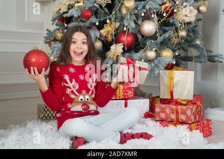 Enfant célébrer Noël à la maison. Traditions d'hiver. Boutique cadeaux concept. Porter le chandail de Noël pour enfants adorables. Bénéficiant d''hiver. Décor d'attributs de Noël. Petite fille près de l'arbre de Noël. Banque D'Images