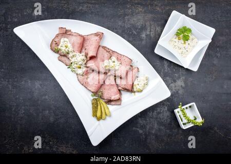 Le déjeuner traditionnel avec des tranches de viande Charcuterie rôti de bœuf et remoulade comme vue de dessus sur une plaque blanche sur fond noir avec l'exemplaire Banque D'Images