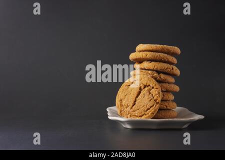 Un cookie de gingembre s'appuie sur une pile de cookies sur une plaque blanche avec un fond noir ; copy space Banque D'Images