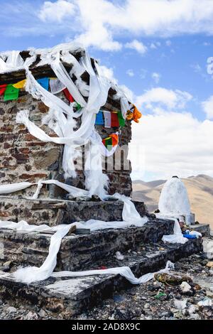 Foulards en soie blanche et les drapeaux de prières l'enrouler dans une colonne en pierre situé dans la vallée du Brahmapoutre de région autonome du Tibet, Chine. Banque D'Images