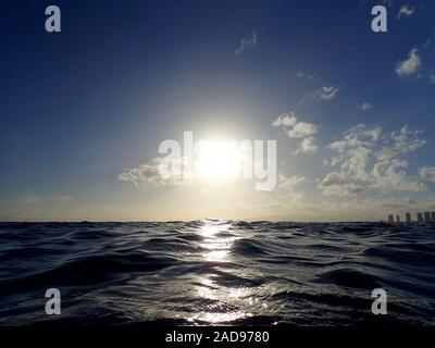 Coucher de soleil sur l'océan avec la lumière se reflétant sur les vagues de l'océan se déplaçant avec des bateaux sur l'eau au loin au large de Waikiki avec nuages sur Oahu, Hawaii. Banque D'Images
