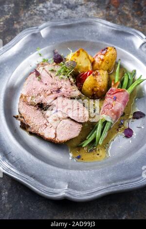 Rôti d'agneau marinées au barbecue avec pommes de terre grecque et les haricots enroulés dans du bacon comme gros plan sur une plaque d'étain Banque D'Images