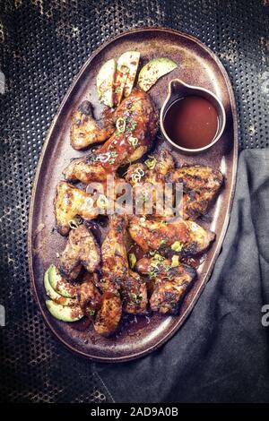 Ailes de poulet barbecue traditionnel et les pilons avec la sauce chili chaud comme vue de dessus sur une plaque Banque D'Images