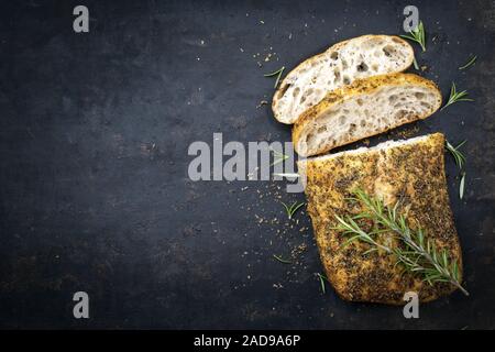 Pain ciabatta italien traditionnel avec des herbes comme vue de dessus sur un vieux tableau noir avec copie espace à gauche Banque D'Images