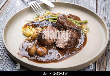 Joues de porc braisé traditionnel allemand en sauce brune avec Swiss rösti et les haricots verts en gros plan sur une plaque au design moderne Banque D'Images