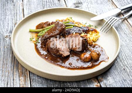 Joues de porc braisé traditionnel allemand en sauce brune avec Swiss rösti et et de haricots verts comme gros plan sur une plaque au design moderne Banque D'Images