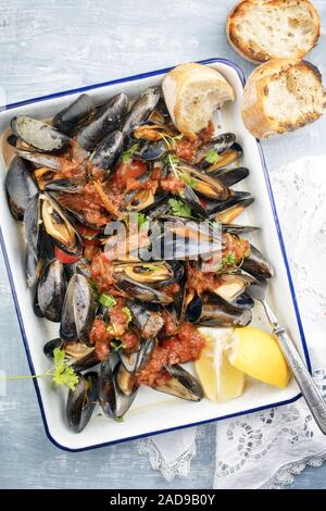 Barbecue traditionnel italien moule bleu avec la baguette et les tomates dans le vin blanc en vue d'en haut sur un plateau Banque D'Images