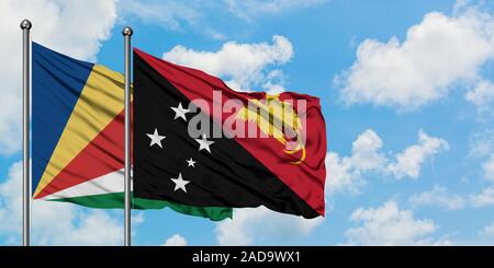Seychelles et de brandir le drapeau de la Papouasie-Nouvelle-Guinée dans le vent contre ciel bleu nuageux blanc ensemble. Concept de diplomatie, de relations internationales. Banque D'Images