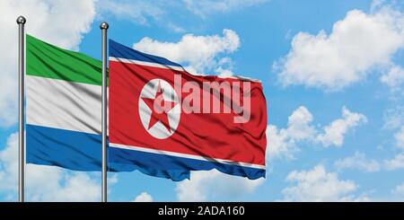 La Sierra Leone et de brandir le drapeau de la Corée du Nord dans le vent contre ciel bleu nuageux blanc ensemble. Concept de diplomatie, de relations internationales. Banque D'Images