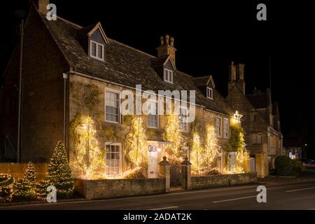 La lumière de l'arbre de Noël les décorations sur l'avant d'une maison et dans les arbres à Broadway à la nuit. Broadway, Cotswolds, Worcestershire, Angleterre. Banque D'Images