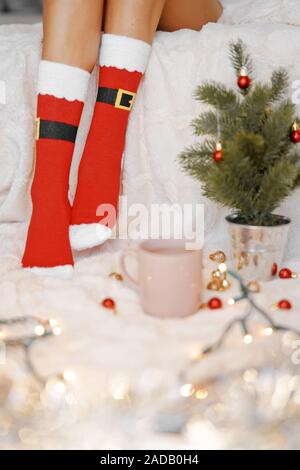 Lifestyle Accueil photo de pieds en chaussettes de noël près de l'arbre de Noël. Femme assise à la couverture, boissons chaudes boissons et détend le réchauffement de leur Banque D'Images