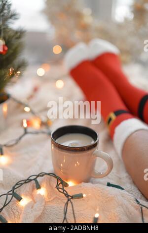 Lifestyle Accueil photo de pieds en chaussettes de noël près de l'arbre de Noël. Femme assise à la couverture, boissons chaudes boissons et détend le réchauffement de leur Banque D'Images