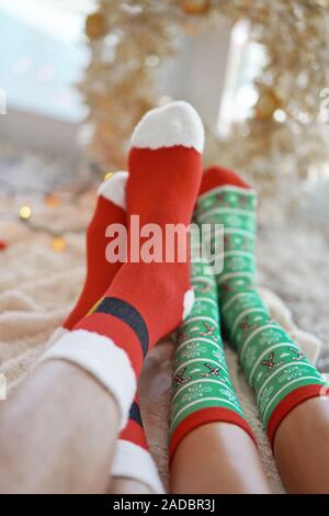 Pieds en chaussettes de noël près de l'arbre de Noël. Couple assis à la couverture, détend réchauffe les pieds dans des chaussettes de laine. L'hiver et Noël h Banque D'Images