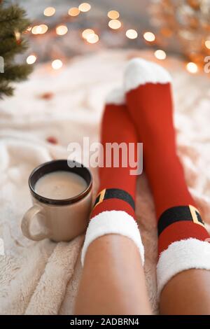 Lifestyle Accueil photo de pieds en chaussettes de noël près de l'arbre de Noël. Femme assise à la couverture, boissons chaudes boissons et détend le réchauffement de leur Banque D'Images