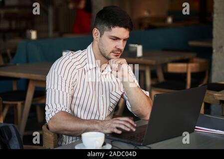 C'est journée ordinaire pour freelancer. Homme adulte est assis dans un café au jour et à l'aide de l'ordinateur portable pour le travail à distance Banque D'Images