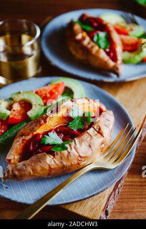Rempli de pommes de terre cuites au four avec des haricots rouge mijotée dans la pâte de tomate servi avec de l'avocat et tomates cerises sur une assiette. Recette de légumes sains. Banque D'Images