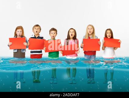 Noyé à la maison. Groupe d'enfants avec des bannières vierge debout dans l'eau de la fonte des glaciers, le réchauffement climatique. L'écologie, de l'environnement concept. Sauver la planète pour les générations futures, arrêter de dénaturer la nature. Banque D'Images